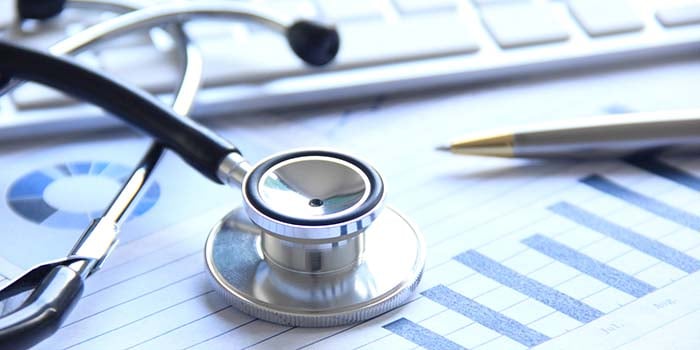 Stethoscope sitting on top of a bar chart, with pen and computer keyboard in background.