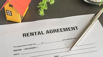 Photo shows a rental contract with a pen on it, and a small toy house above it.