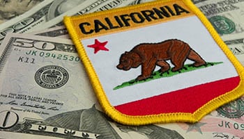 Photo of $50 and $100 bills and a patch sitting on top that says "California" and has the bear and a red star on it.