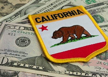 Photo of $50 and $100 bills and a patch sitting on top that says "California" and has the bear and a red star on it.