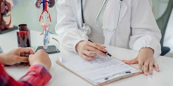 Photo of a doctor speaking with somebody at a desk, pointing to a clip-board.