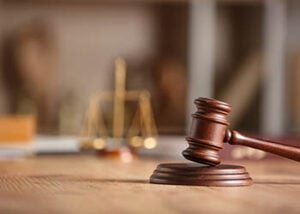 Photo zoomed in on a judge's gavel with scales of justice in the background.