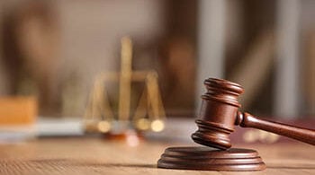 Photo zoomed in on a judge's gavel with scales of justice in the background.