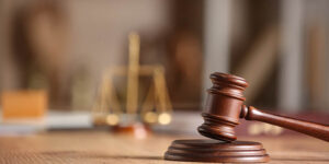 Photo zoomed in on a judge's gavel with scales of justice in the background.