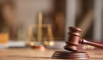Photo zoomed in on a judge's gavel with scales of justice in the background.