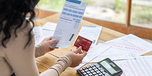 Photo of a woman holding a letter and credit card. On her desk are debt collection letters and a calculator