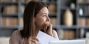 A woman holds a piece of paper, looking pensive and stressed.