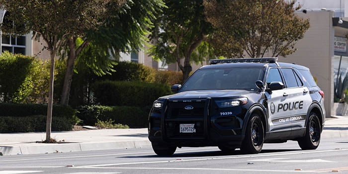 Photograph of a City of Corona police vehicle on a street with trees.