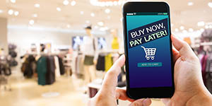 Photo shows a person in a clothes store, holding a cell phone that says "buy now, pay later" with a shopping cart icon