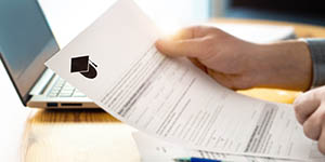 person holding a piece of paper (like an application) with a graduation cap on the top of the page.