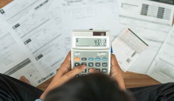 Photo of a person typing numbers on a calculator with bills underneath.