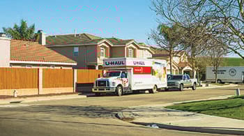 A Uhaul rental truck is parked on a neighborhood street, along with a truck, and a larger moving truck in the background.