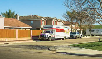 A Uhaul rental truck is parked on a neighborhood street, along with a truck, and a larger moving truck in the background.