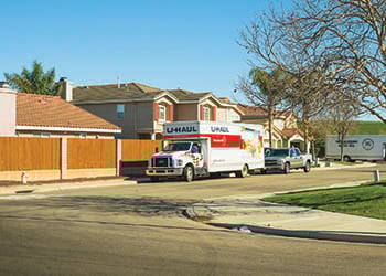 A Uhaul rental truck is parked on a neighborhood street, along with a truck, and a larger moving truck in the background.