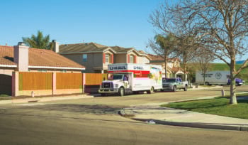 A Uhaul rental truck is parked on a neighborhood street, along with a truck, and a larger moving truck in the background.