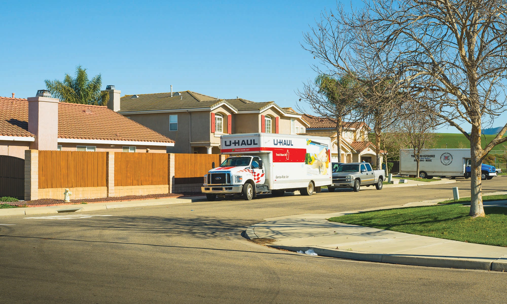 A Uhaul rental truck is parked on a neighborhood street, along with a truck, and a larger moving truck in the background.