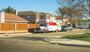 A Uhaul rental truck is parked on a neighborhood street, along with a truck, and a larger moving truck in the background.