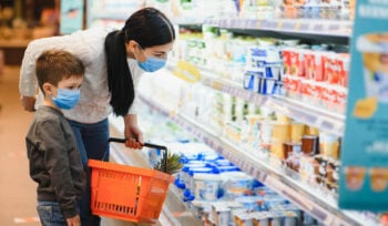 A woman wearing a mask is shopping in a grocery store with her son, who is also masked.