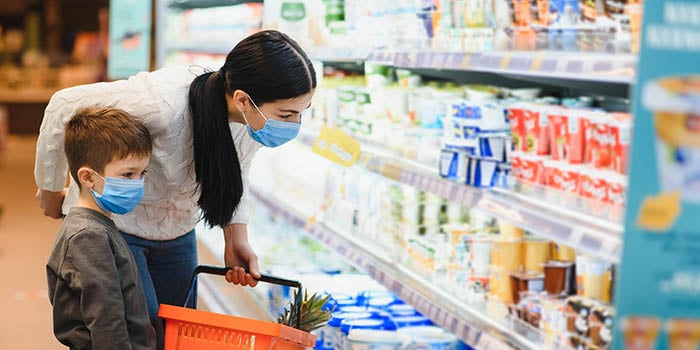 A woman wearing a mask is shopping in a grocery store with her son, who is also masked.