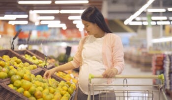 Photo of a pregnant woman shopping in the fruit section of a grocery store.