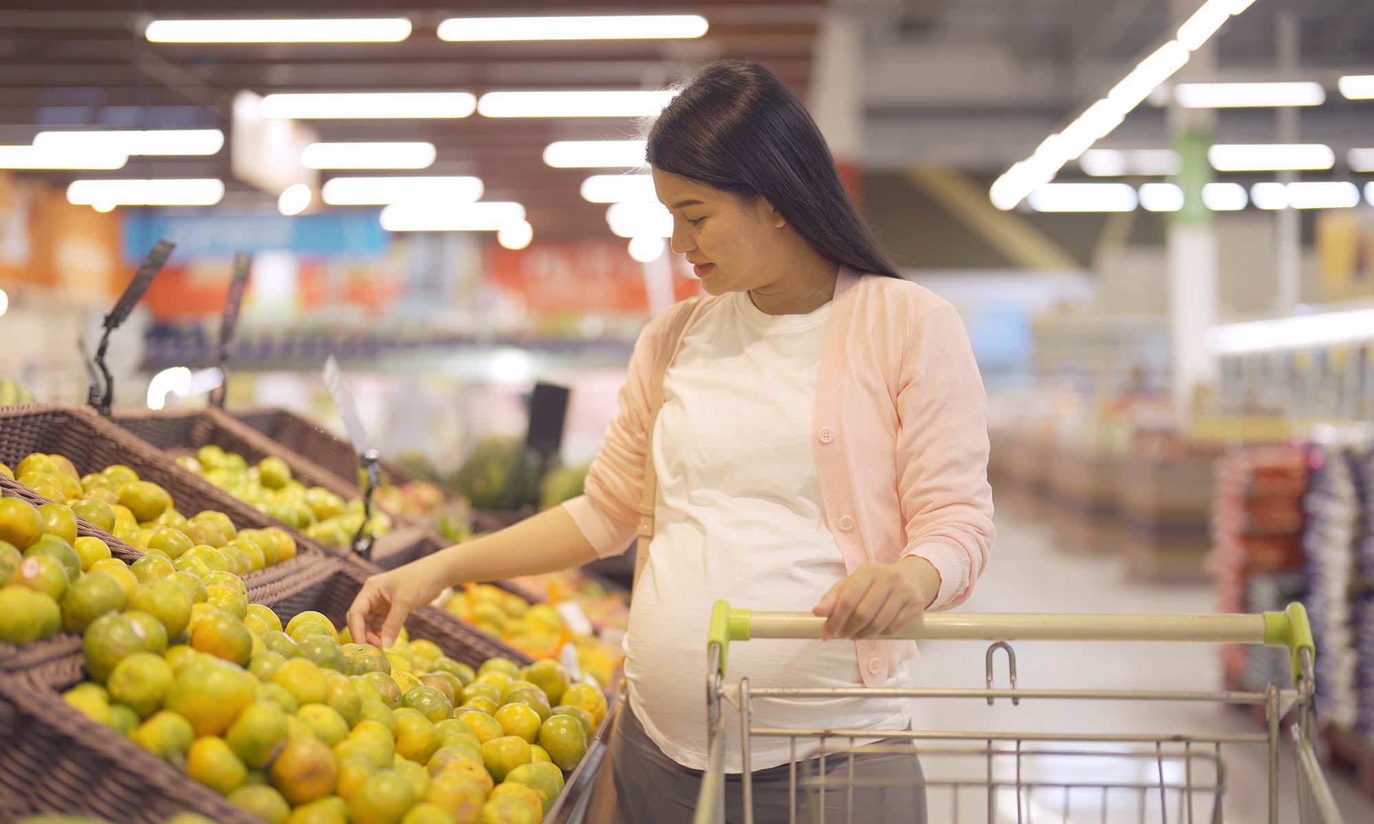 Photo of a pregnant woman shopping in the fruit section of a grocery store.