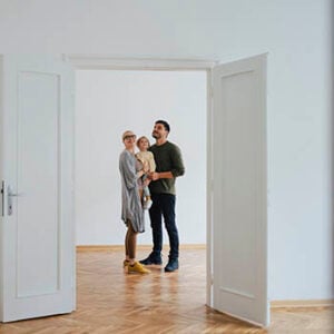 Photograph of a woman holding a small child next to a man. They are indoors, looking at an open door.