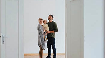 Photograph of a woman holding a small child next to a man. They are indoors, looking at an open door.