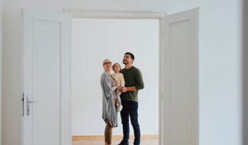 Photograph of a woman holding a small child next to a man. They are indoors, looking at an open door.