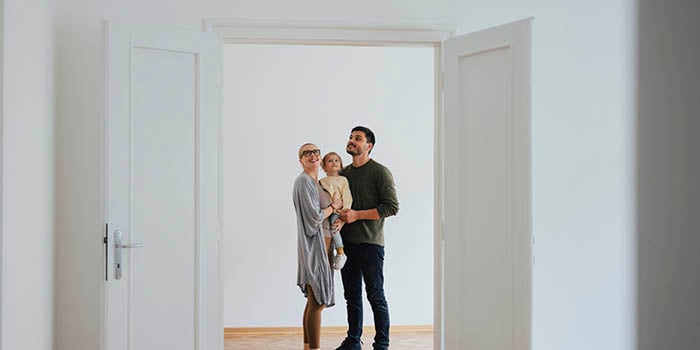 Photograph of a woman holding a small child next to a man. They are indoors, looking at an open door.