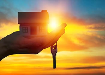 Picture shows a hand holding a home and a key with a sunset in the background