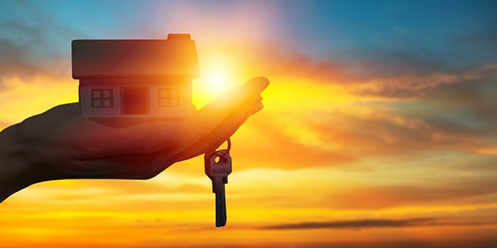 Picture shows a hand holding a home and a key with a sunset in the background